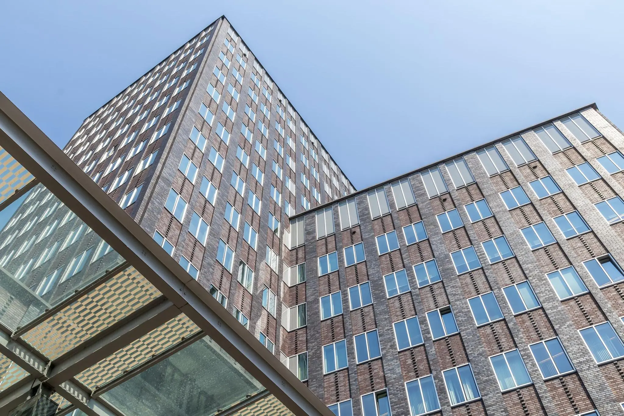 Hoogbouw aan de Barbara Strozzilaan met moderne gevel van baksteen en glas tegen een heldere blauwe lucht.